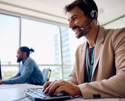 Happy employee with headset working on computer in office.